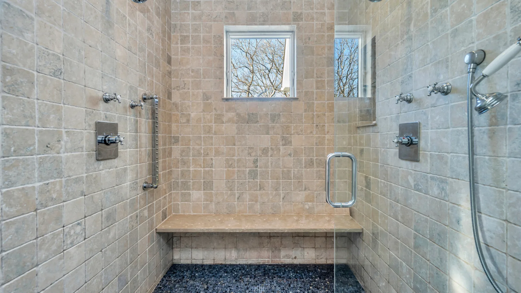 Una zona de ducha con azulejos, un banco integrado y una ventana.