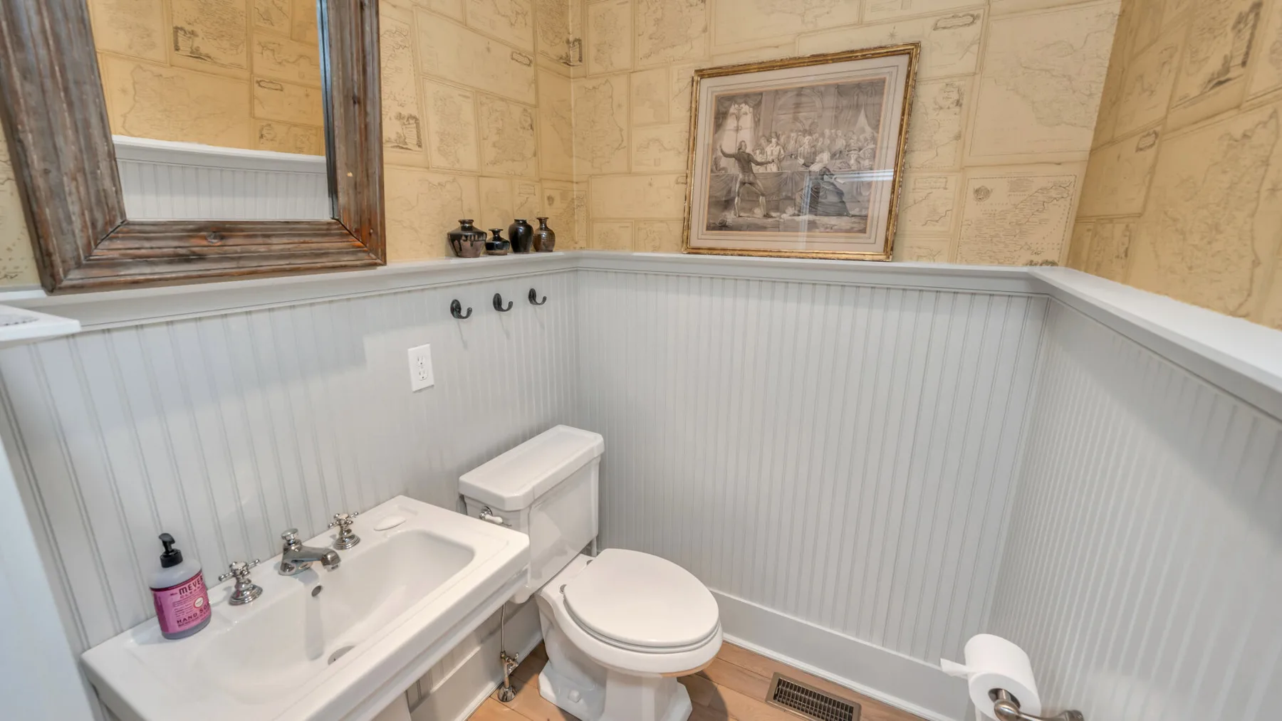 Un baño con lavabo e inodoro, paredes claras con paneles y una imagen enmarcada.