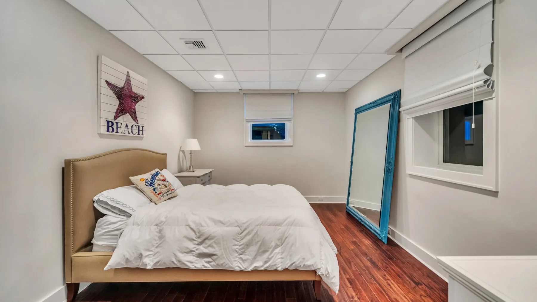 Un dormitorio con una cama vestida con ropa de cama blanca y un espejo alto con marco azul.