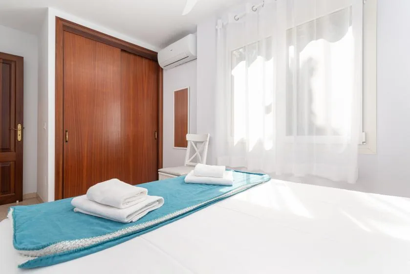 Un dormitorio luminoso con una cama, toallas dobladas y un armario grande de madera.
