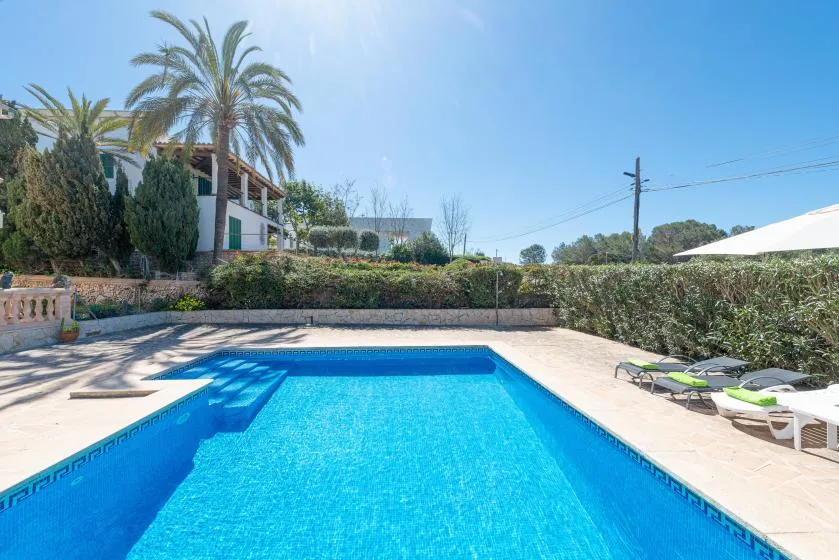 Una piscina al aire libre está rodeada por una terraza pavimentada y asientos de descanso.