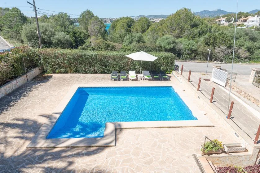 Una piscina al aire libre está en un patio pavimentado junto a tumbonas y una sombrilla.