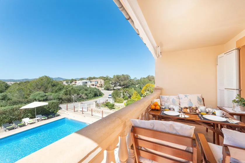Un comedor en un balcón cubierto da a una piscina y colinas verdes.