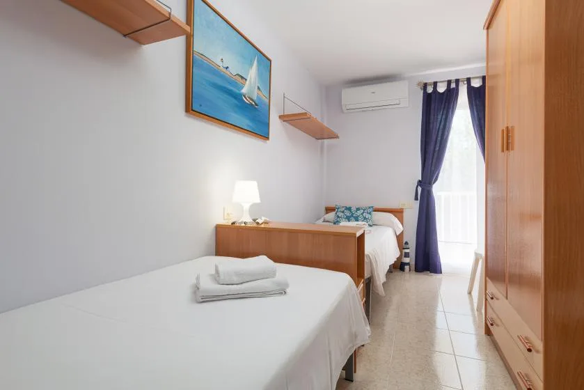 Un dormitorio luminoso con dos camas, un armario y una ventana con cortinas.