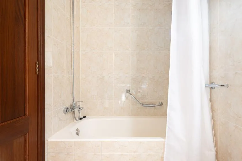 Un baño con azulejos, bañera y cortina de ducha blanca.