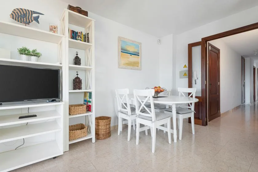 Una luminosa zona de comedor y estar con una mesa blanca y un televisor.