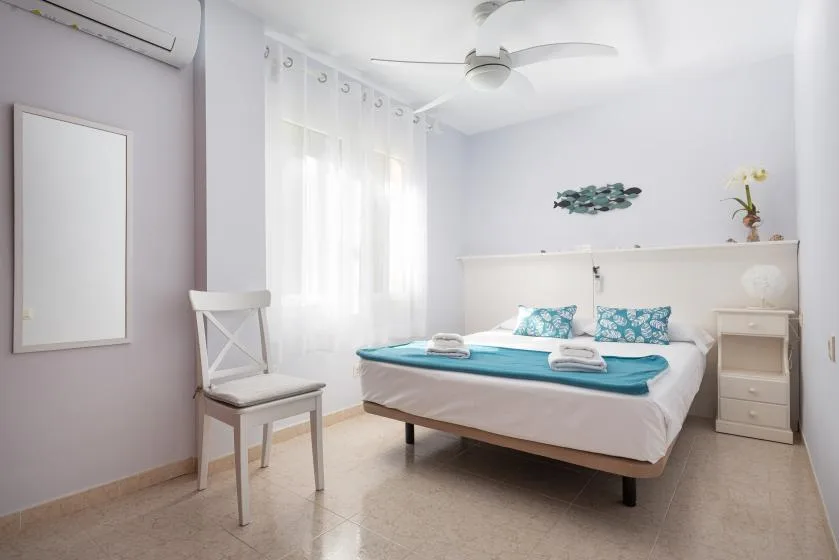 Un dormitorio luminoso con una cama, mesitas de noche y cortinas translúcidas.