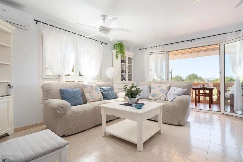 Una sala luminosa con asientos y una mesa de centro junto a grandes puertas de vidrio.