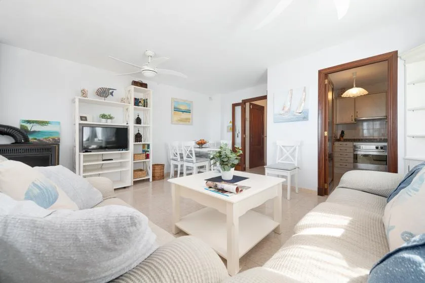 Una sala luminosa con asientos alrededor de una mesa de centro blanca y un comedor abierto.