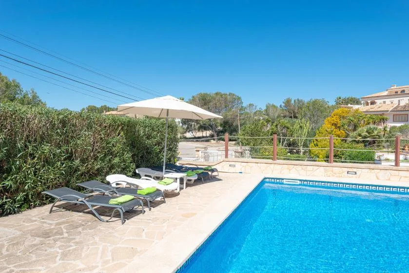Una piscina al aire libre junto a un patio pavimentado con tumbonas y una sombrilla.