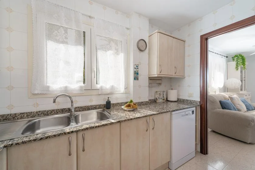 Una cocina luminosa con fregadero bajo ventanas con cortinas de encaje y una encimera.