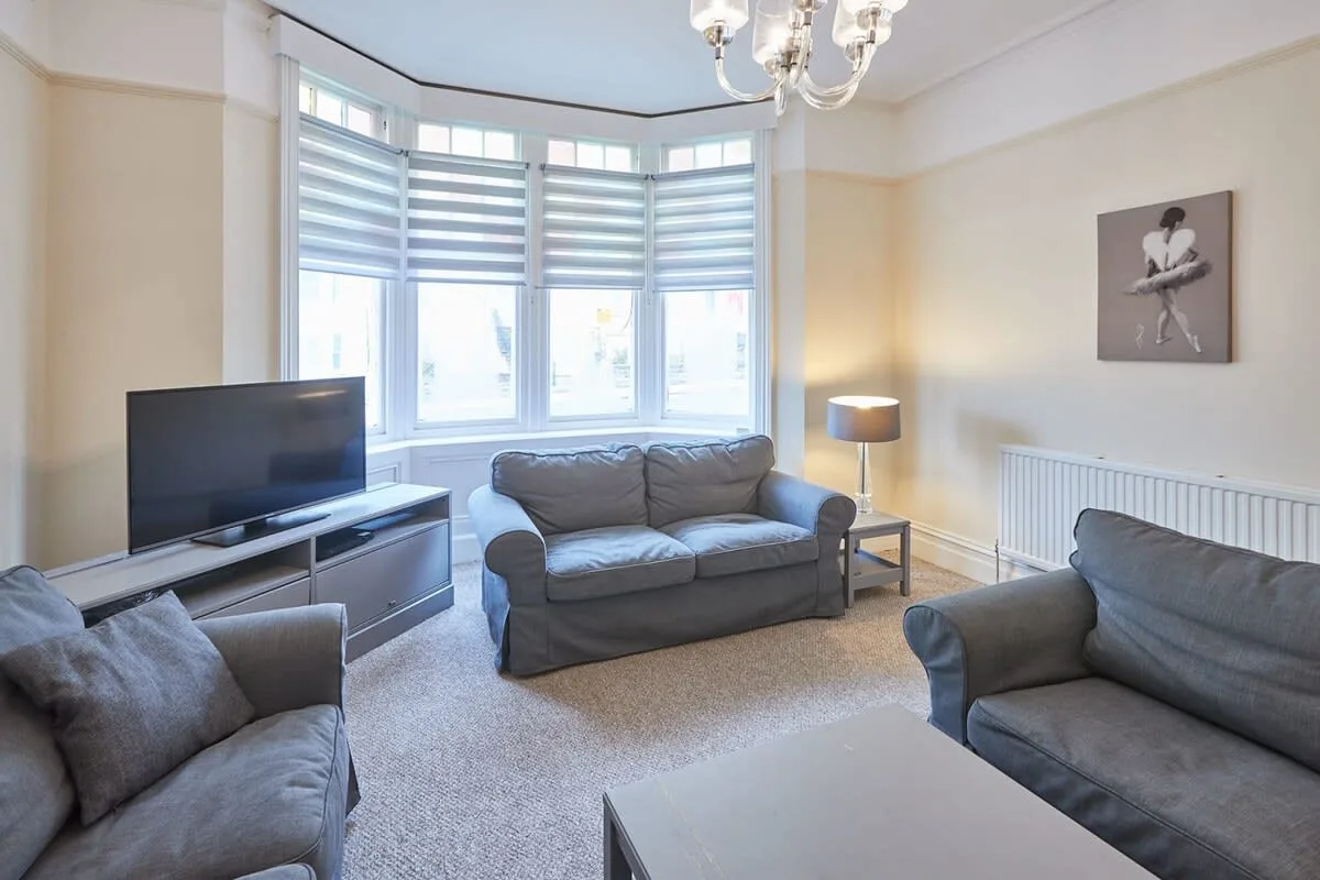A living room with gray seating, a television, and a large bay window.