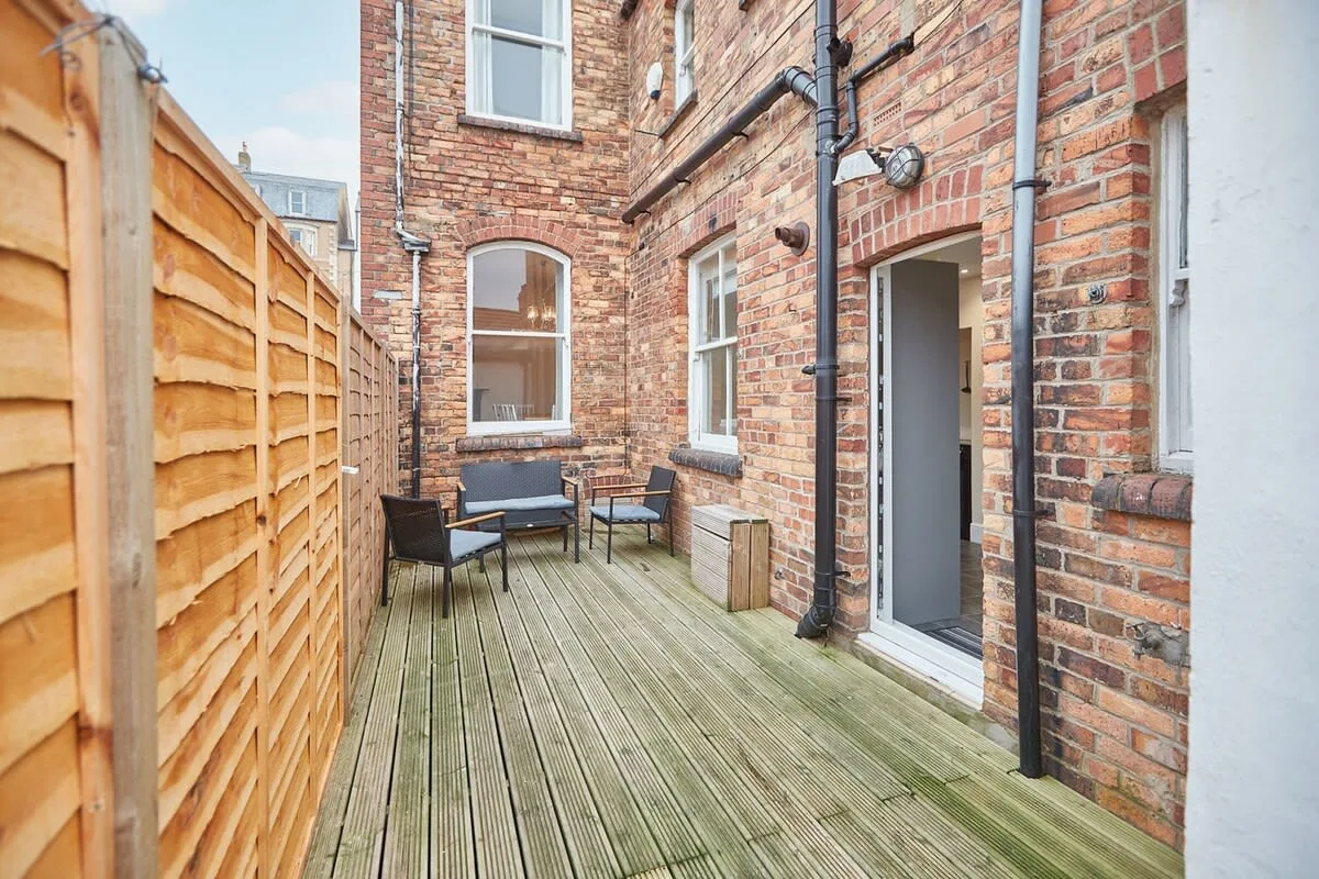 A brick courtyard with wooden decking, outdoor seating, and a fence.