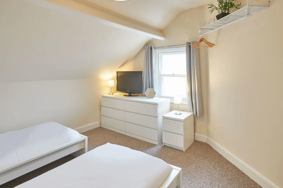 A bright bedroom with two beds, a dresser, and a window.