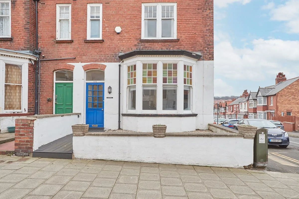 A red-brick townhouse facade with green and blue doors and a bay window.