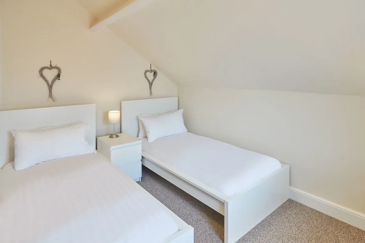 A bright bedroom with two single beds and a bedside lamp.