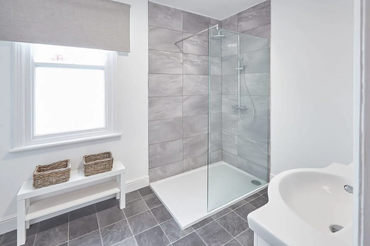 A tiled bathroom with a glass shower, window, and sink.