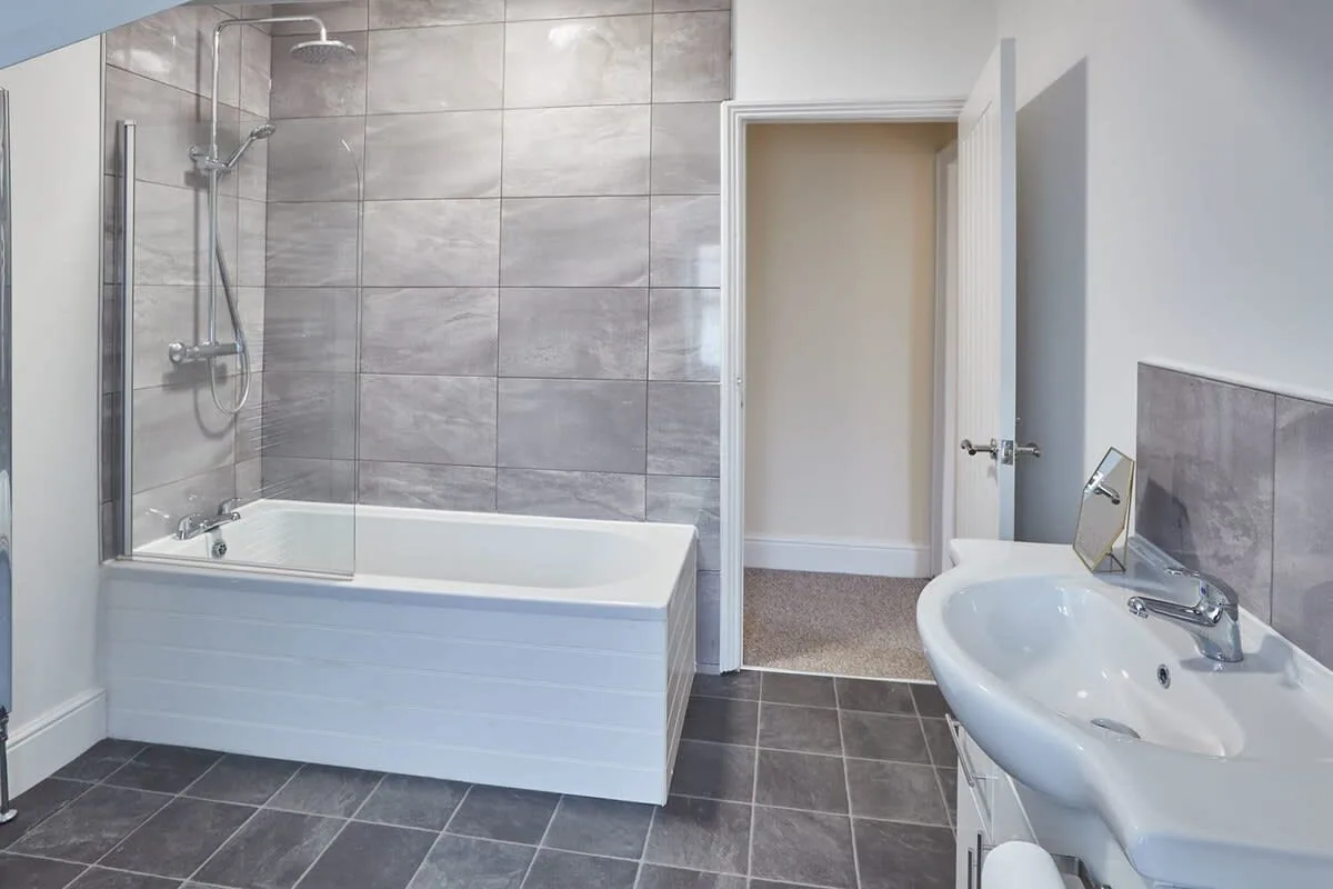 A bathroom with a tiled bathtub and a sink beside the open doorway.