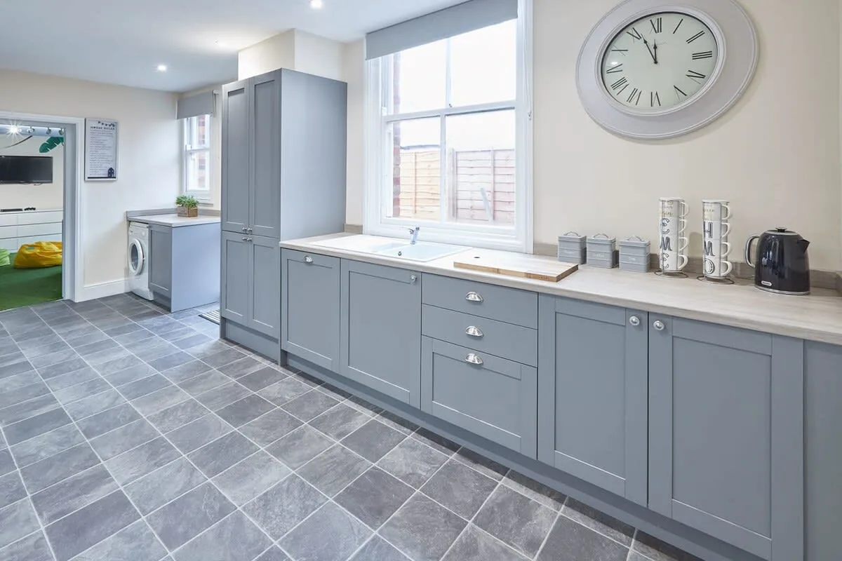 A bright kitchen with gray cabinets, a large window, and a tiled floor.