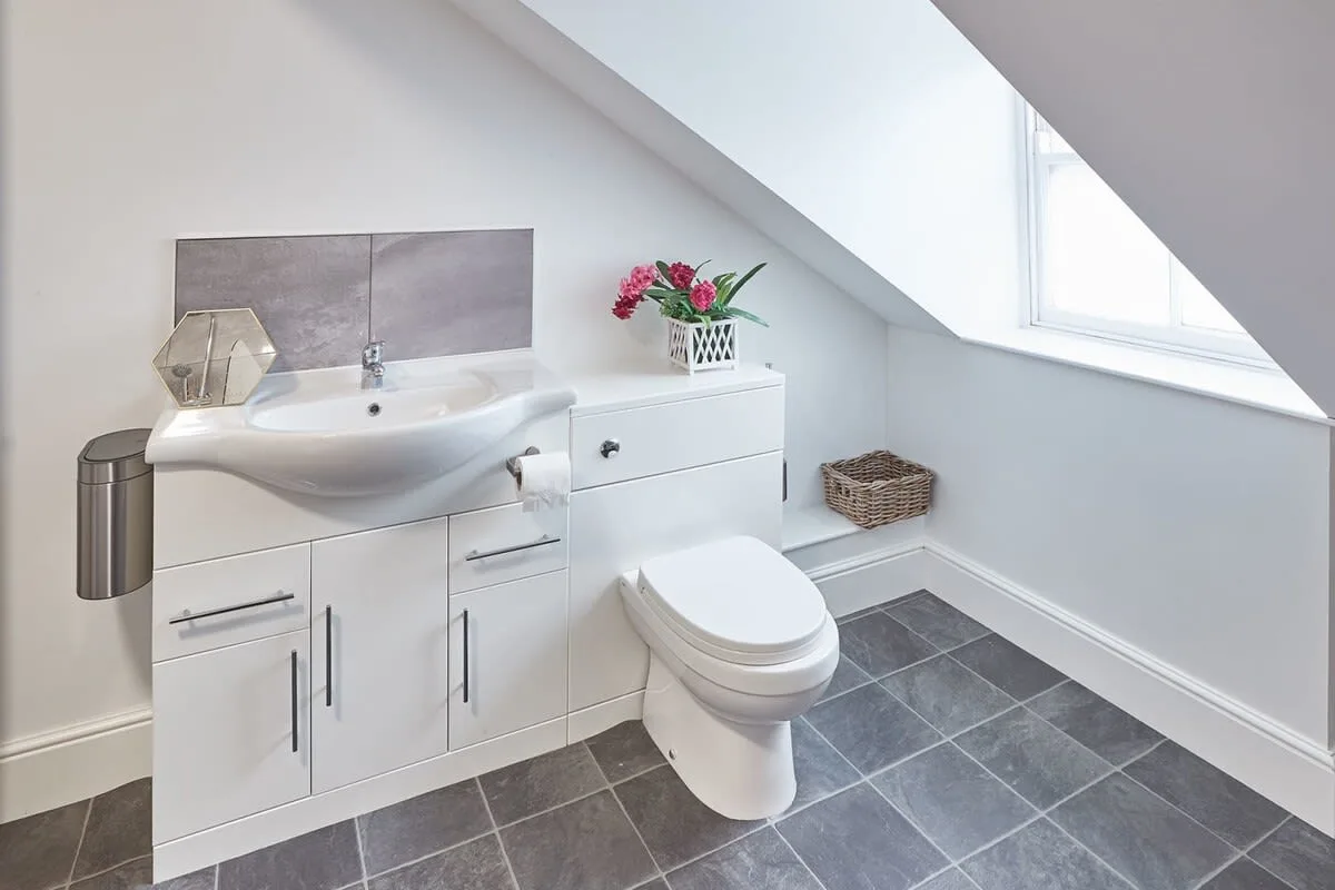 A bathroom with a sink, vanity, and toilet beneath a sloped ceiling.