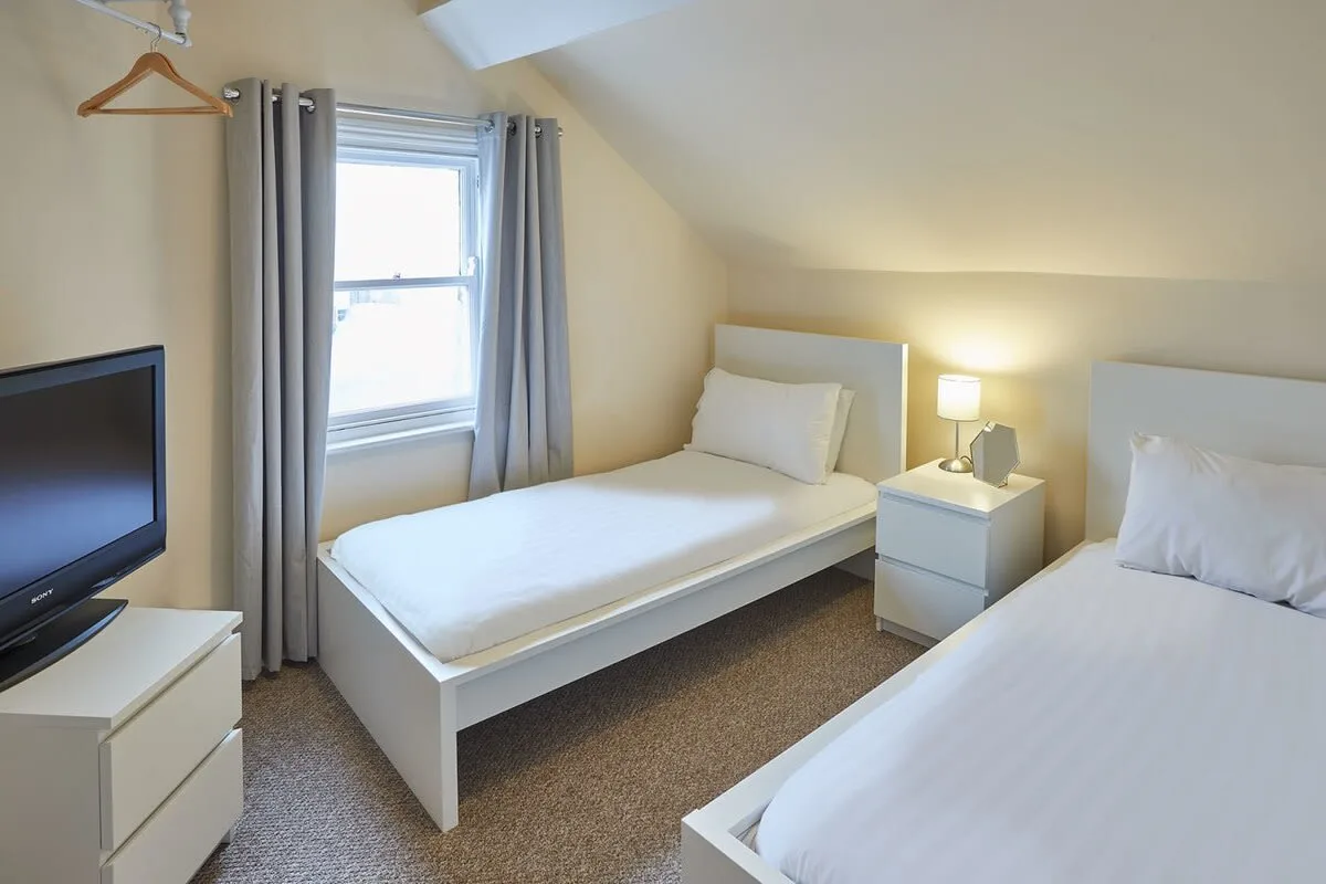 A bedroom with two single beds, a television, and a window.