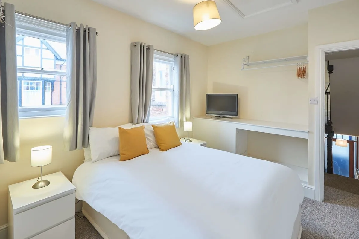 A bedroom with a bed, curtained windows, and a television on a desk.