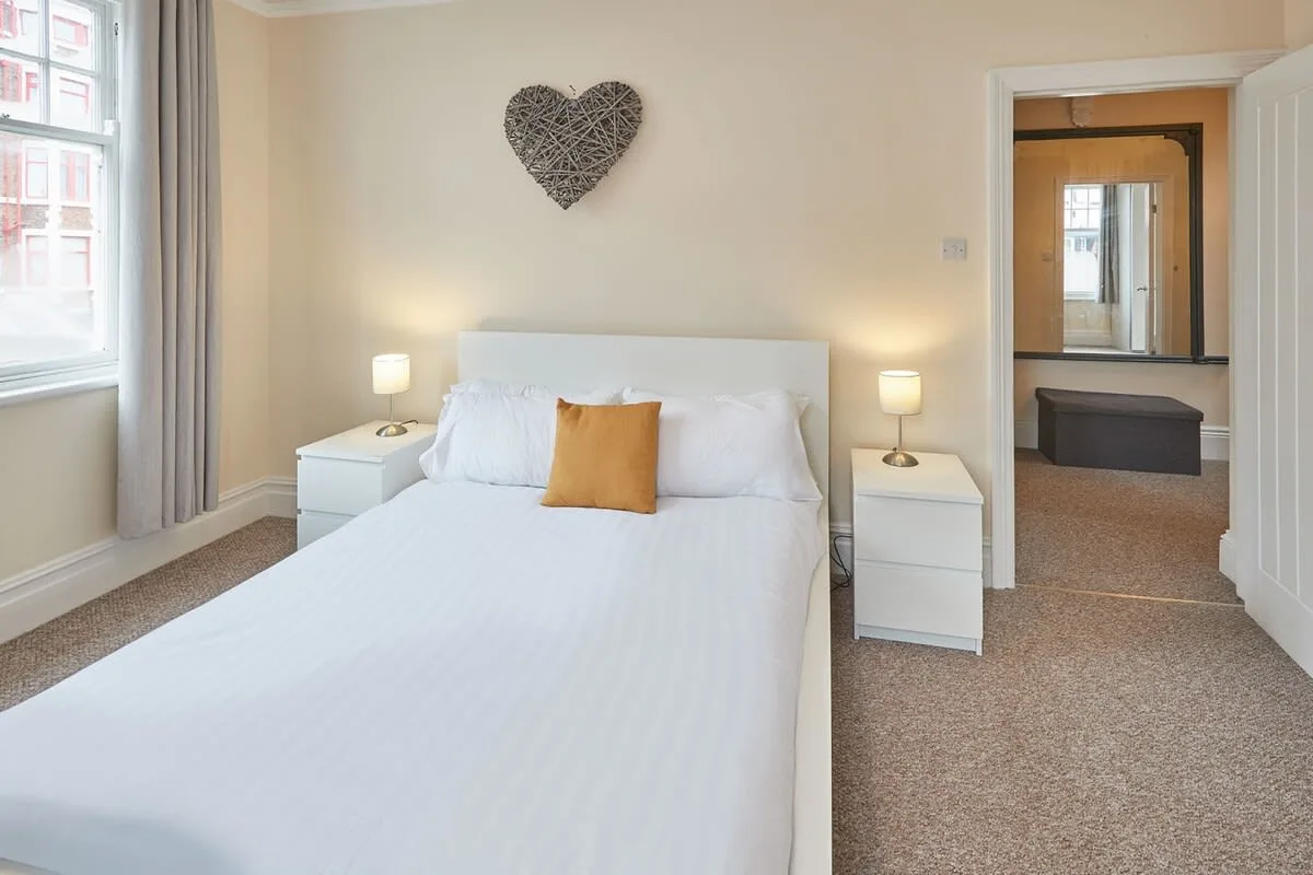 A bright bedroom with a neatly made bed and windows along one wall.