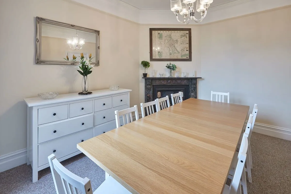 A dining room with a long wooden table and white seating.