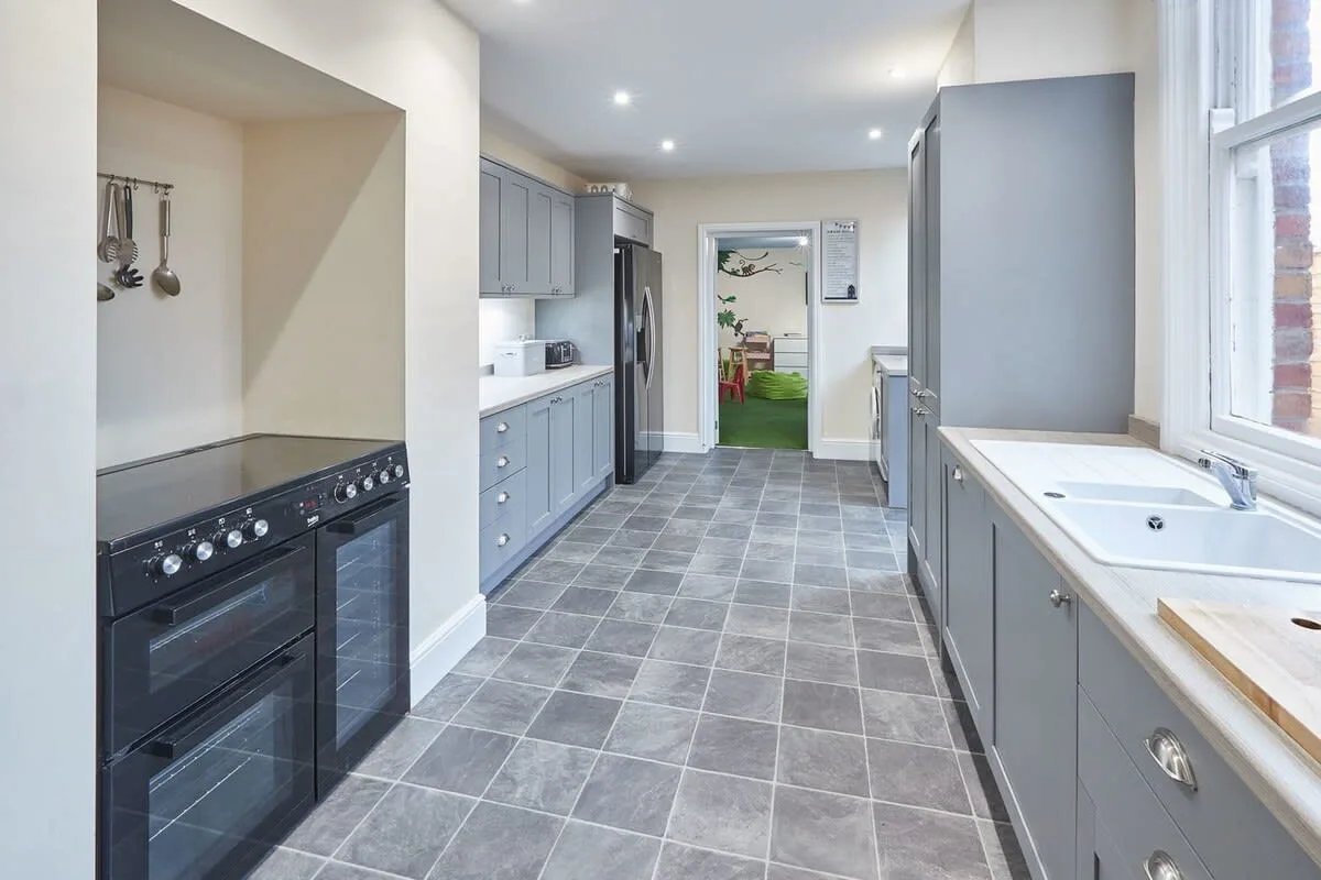A galley kitchen with gray cabinetry, a dark range, and a long sink counter.