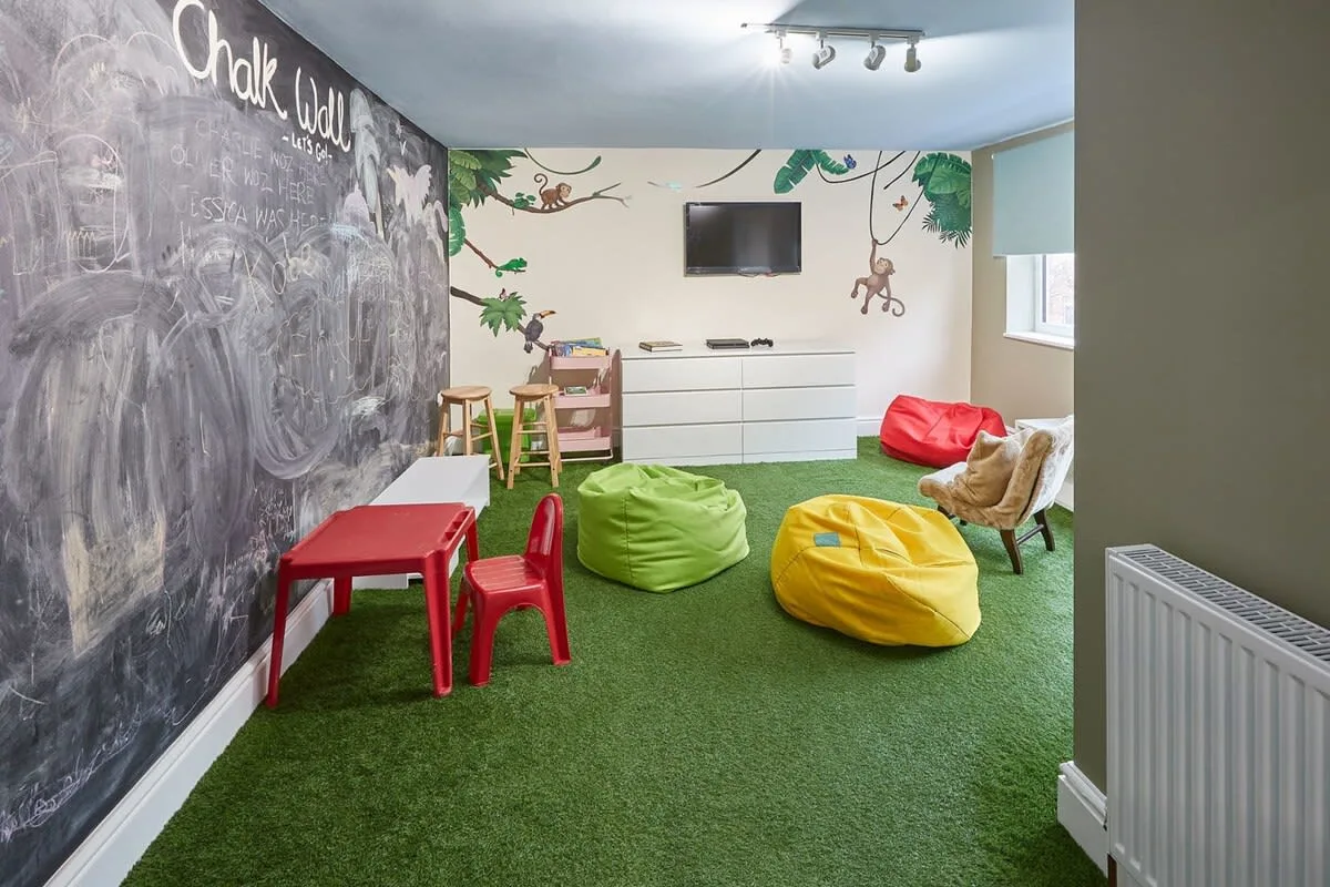 A colorful playroom has a chalkboard wall, floor cushions, and a television.