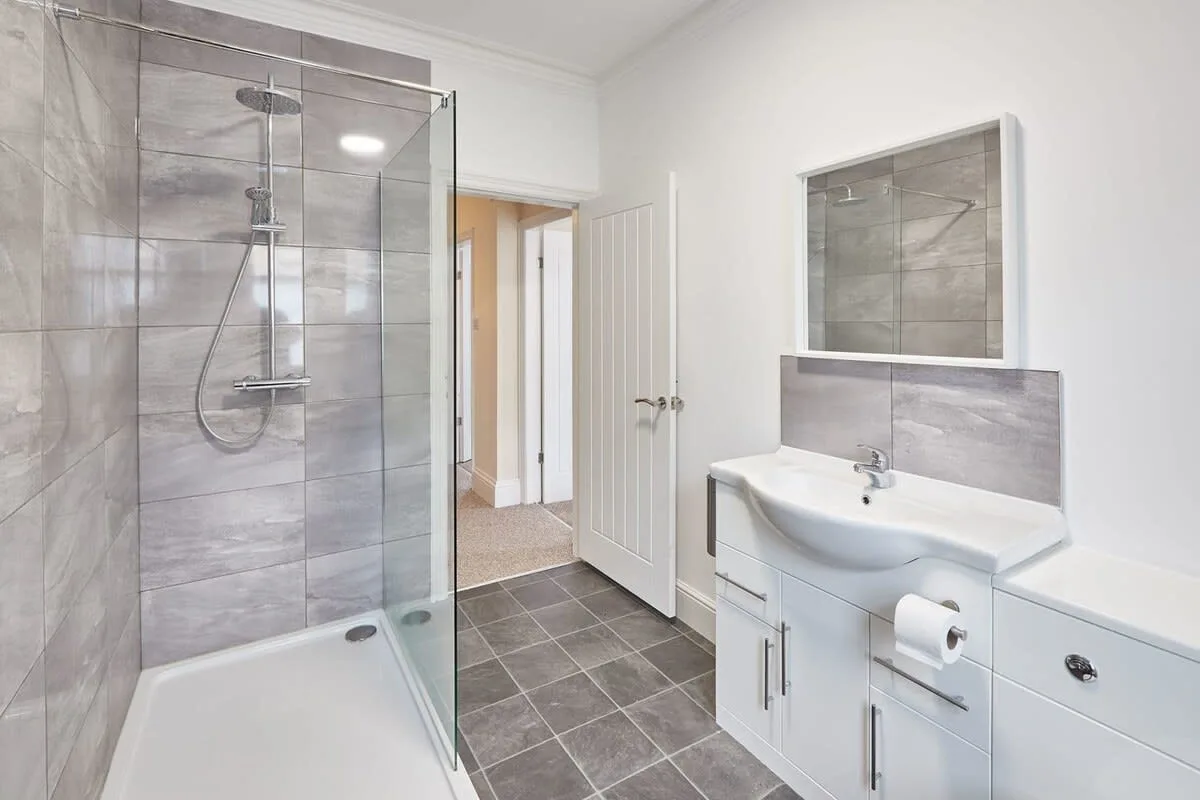 A bathroom with a glass shower, sink, and wall mirror.