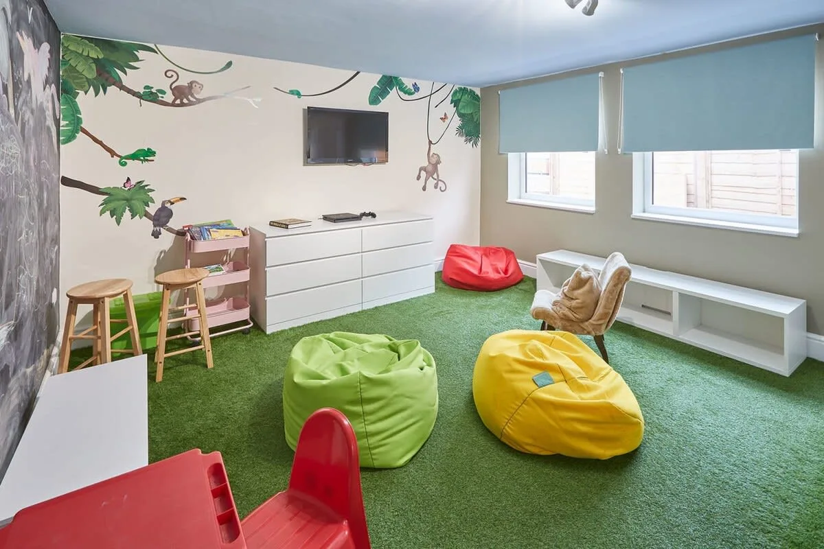 A colorful playroom has green flooring, beanbag seating, and a wall mural.