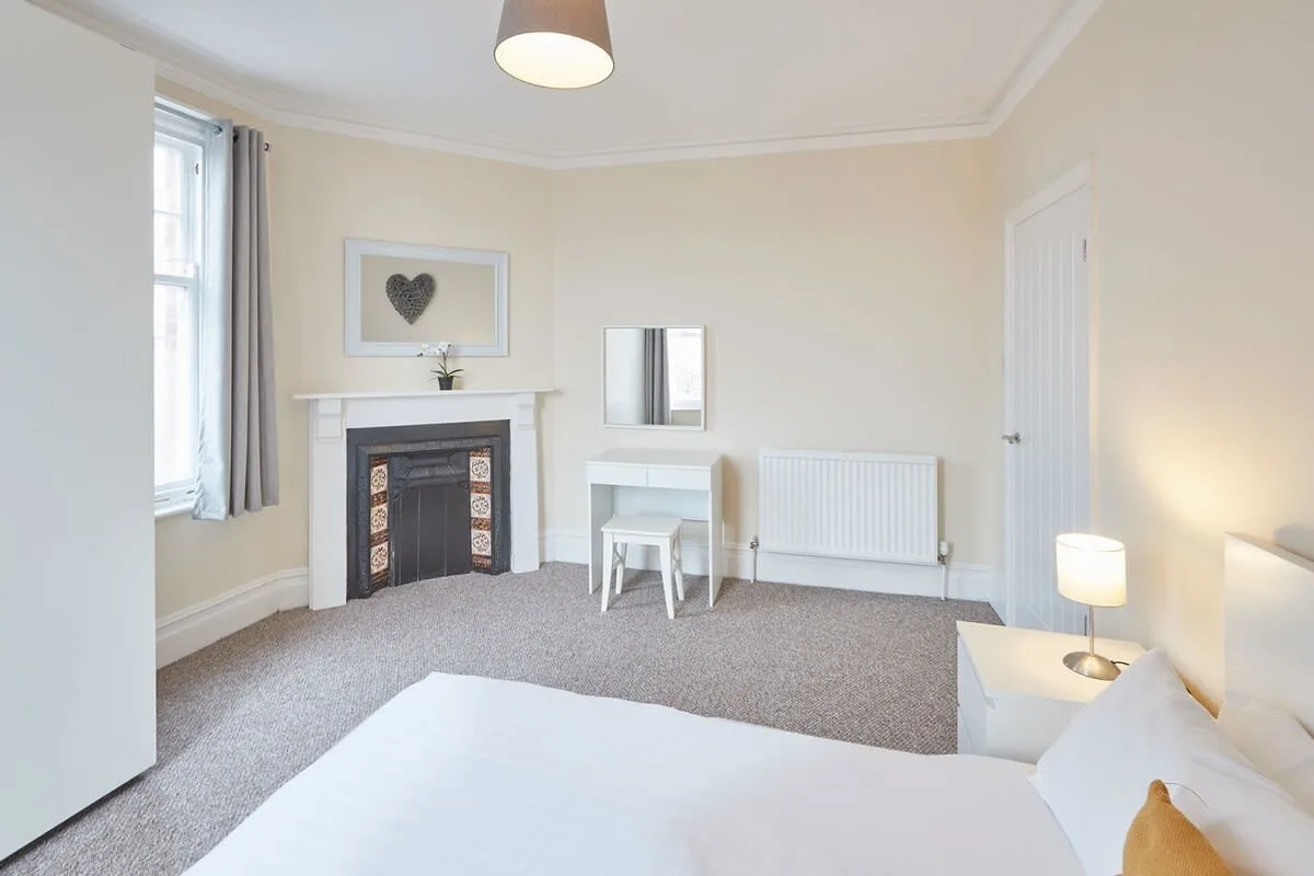 A bright bedroom with a fireplace, bedside table, and white bedding.
