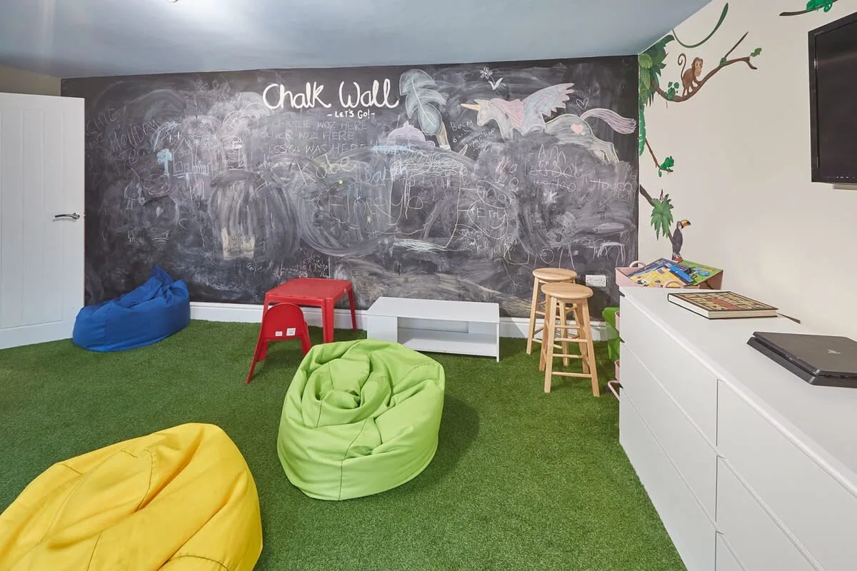 A children's playroom has a chalkboard wall, beanbag seating, and a small table.