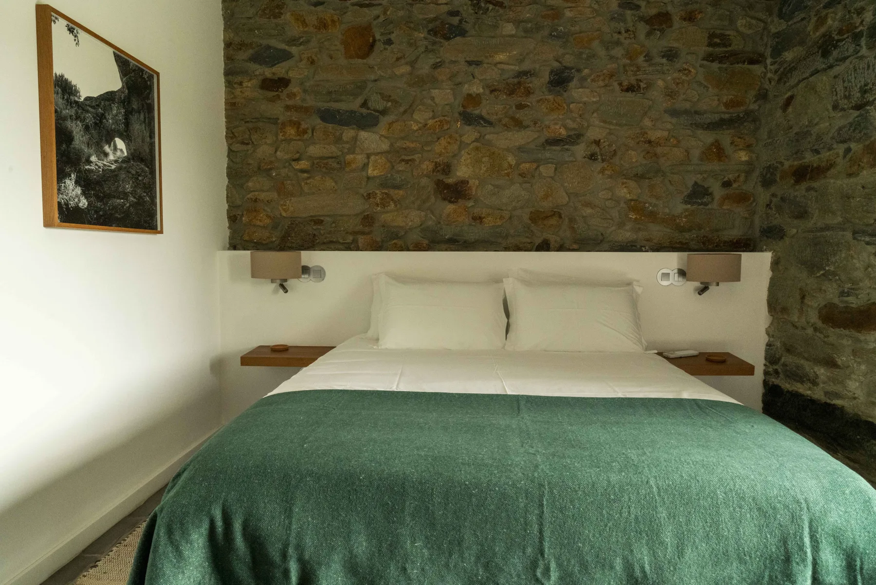 Un dormitorio con una cama cubierta por una manta verde frente a una pared de piedra.
