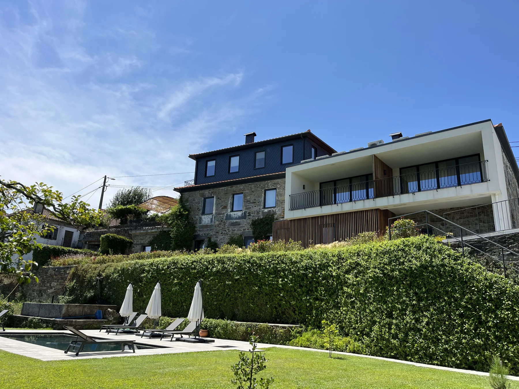 Una casa en la ladera con balcones da a un jardín y una piscina exterior.