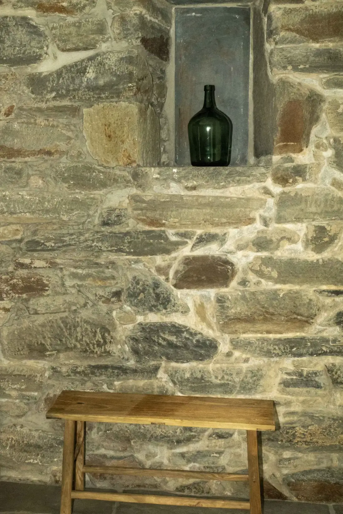 Una pared de piedra con un nicho empotrado y un banco de madera.