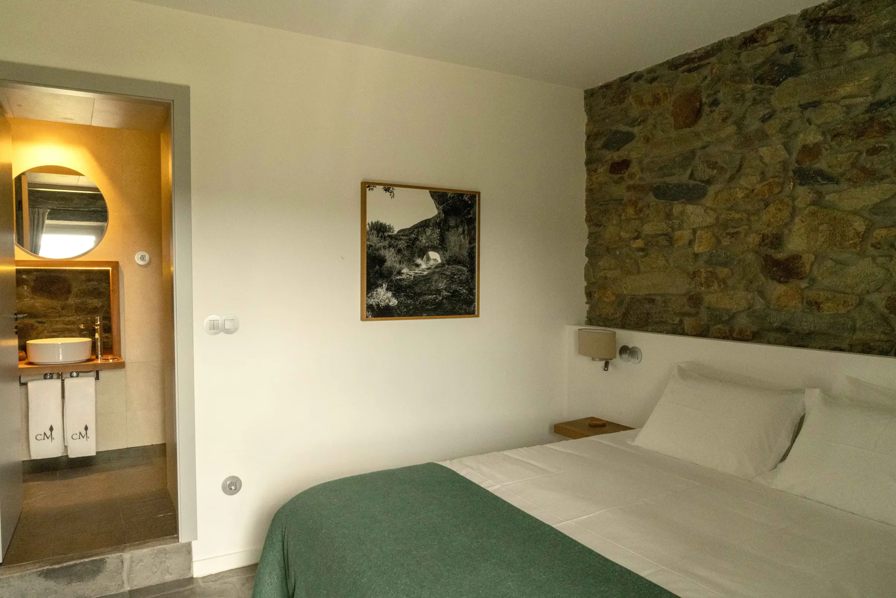 Un dormitorio con una cama junto a una pared de piedra y una puerta abierta al baño.