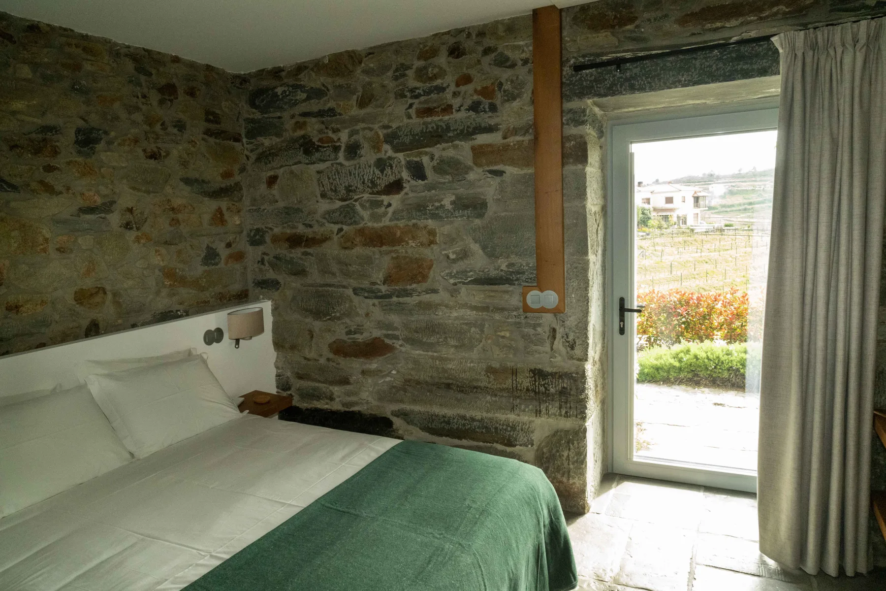 Un dormitorio con una cama tendida junto a una puerta de cristal que da a la vegetación.