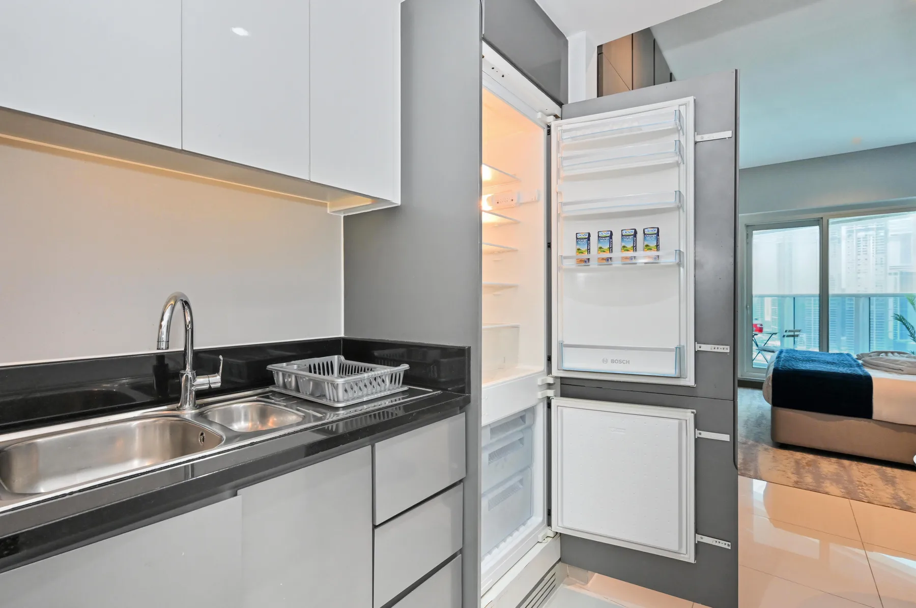 Una cocina compacta con fregadero y refrigerador abierto.