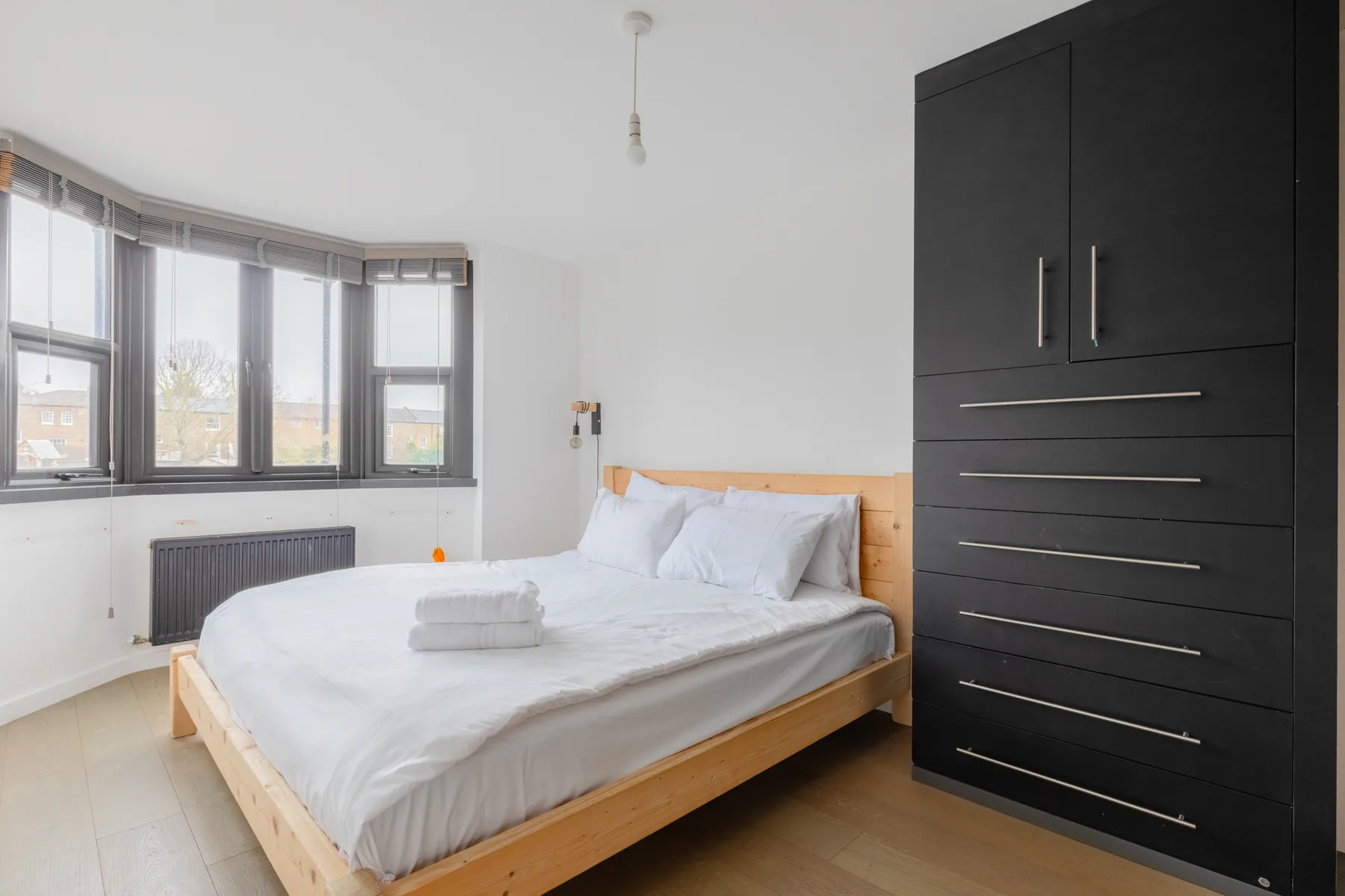 Un dormitorio luminoso con una cama junto a una gran ventana esquinera.