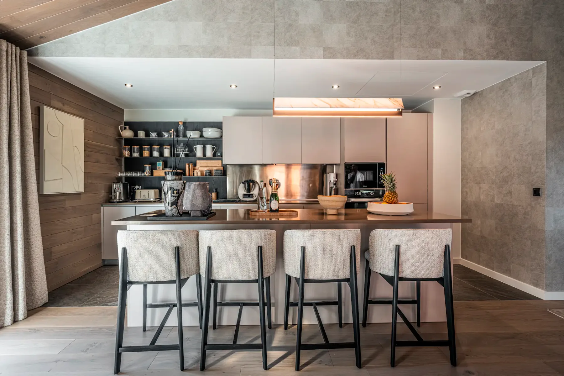 Modern kitchen with a large island, barstools, open shelves, and pendant lighting. Neutral tones and wooden accents create a cozy atmosphere.
