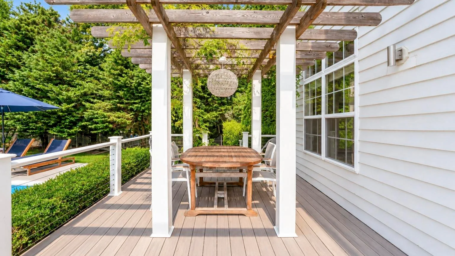 Un comedor exterior cubierto con una mesa de madera bajo una pérgola.