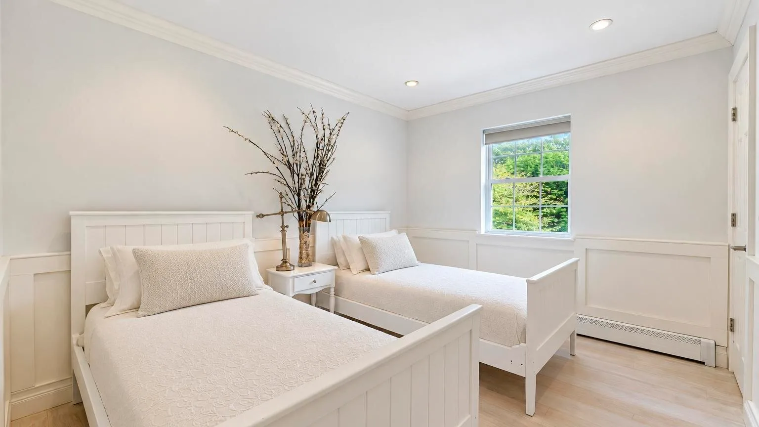 Un dormitorio luminoso con dos camas y una ventana con vistas a la vegetación.