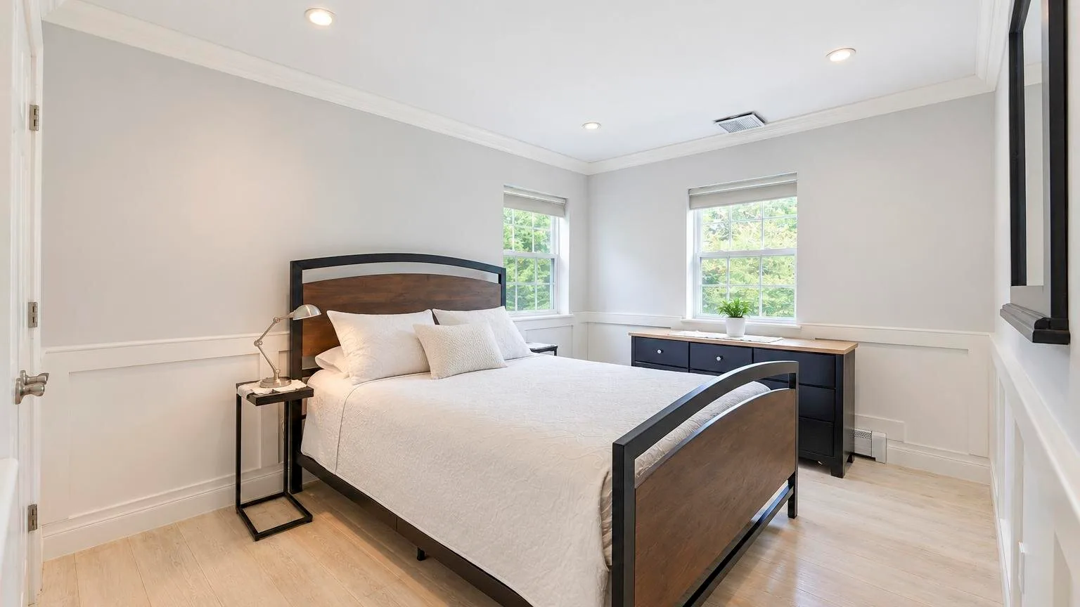 Un dormitorio luminoso con una cama bien tendida y dos ventanas.