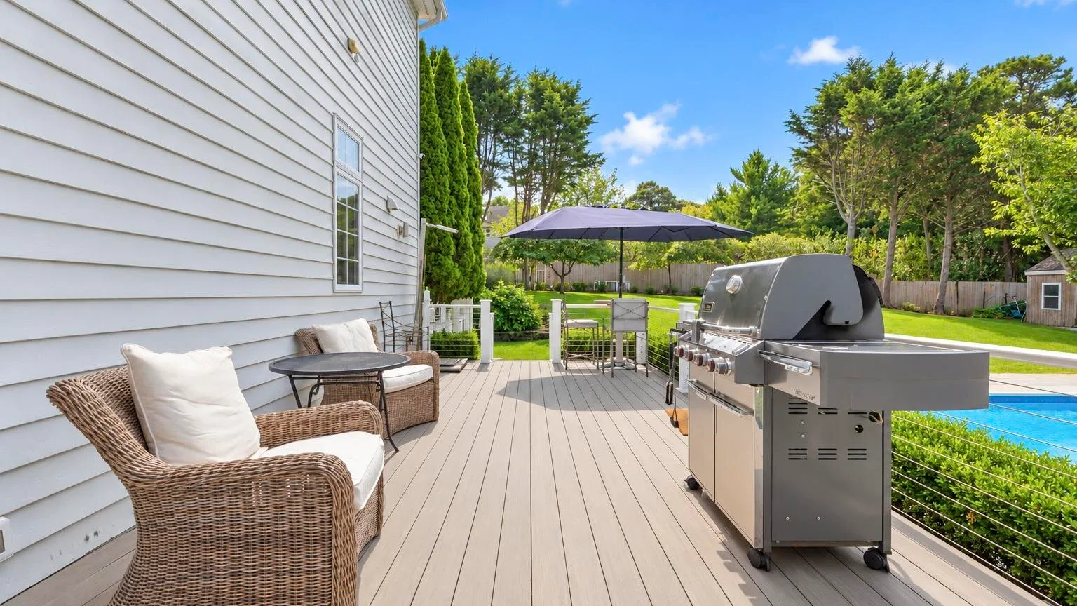 Una terraza exterior con asientos, una parrilla y una sombrilla junto a la casa.