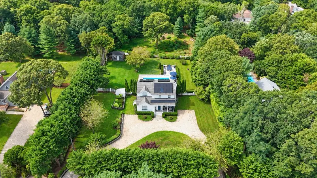Una vista aérea muestra una casa y una entrada rodeadas de árboles y vegetación.