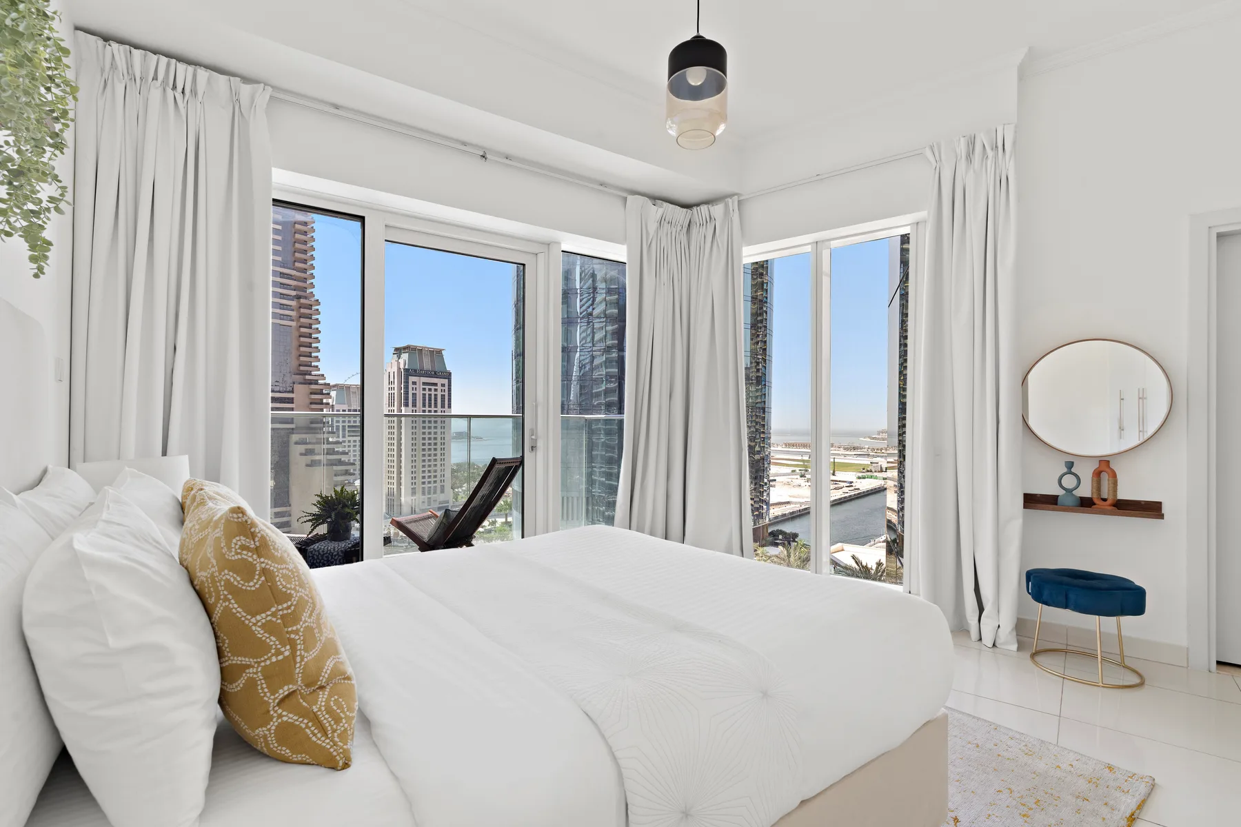 A bright bedroom with a large bed beside windows overlooking the city.