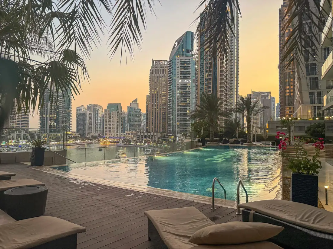 A rooftop swimming pool overlooks a city skyline at sunset.