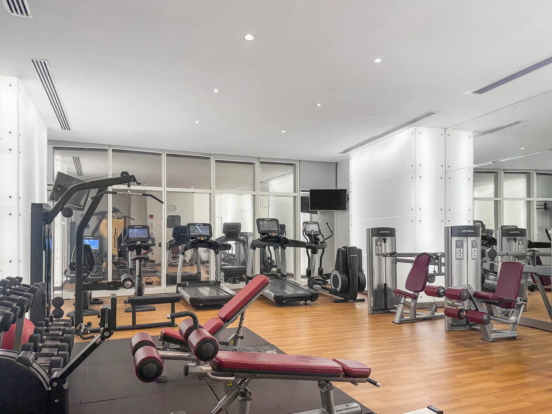 A gym with exercise machines and weight benches on a wood floor.
